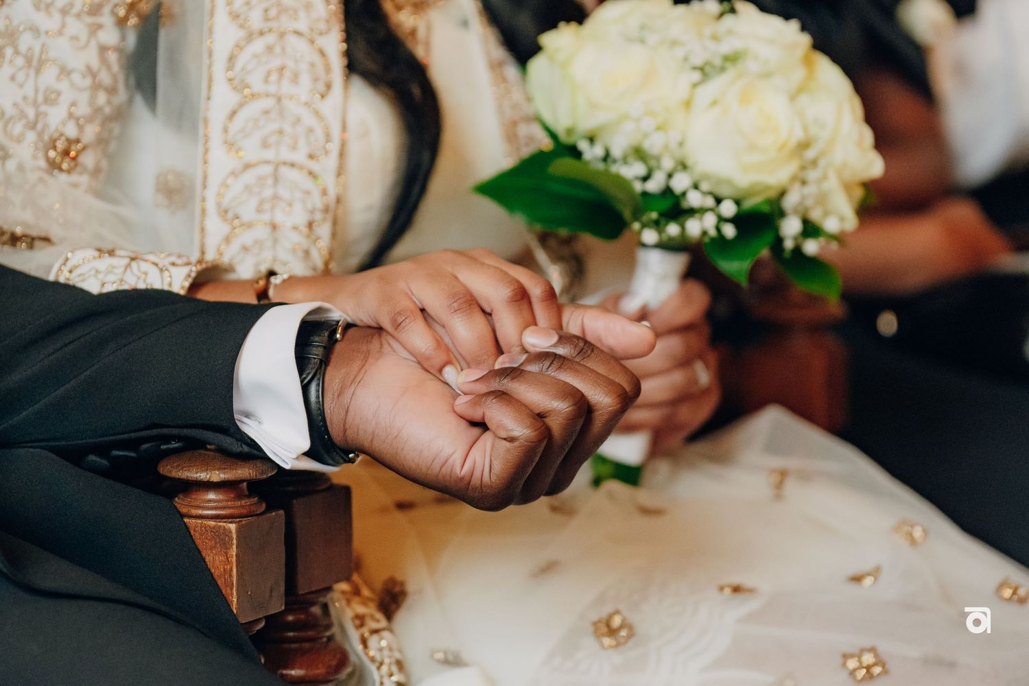 Close up of hands being held during a wedding ceremony with white roses in the background.