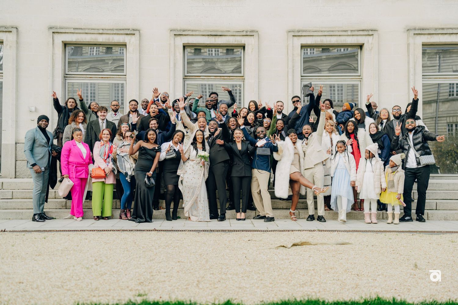Large wedding party poses for group photo on stone steps wearing mix of formal attire and bright colors.