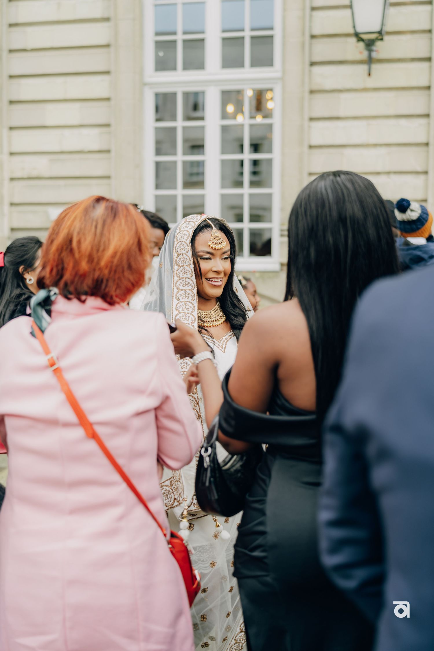 Wedding guests gather around the bride outside an elegant building for celebrations.