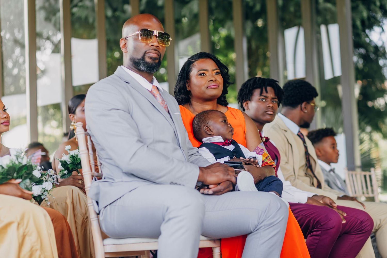 Wedding guests in formal attire seated at an outdoor ceremony with a baby in their midst.