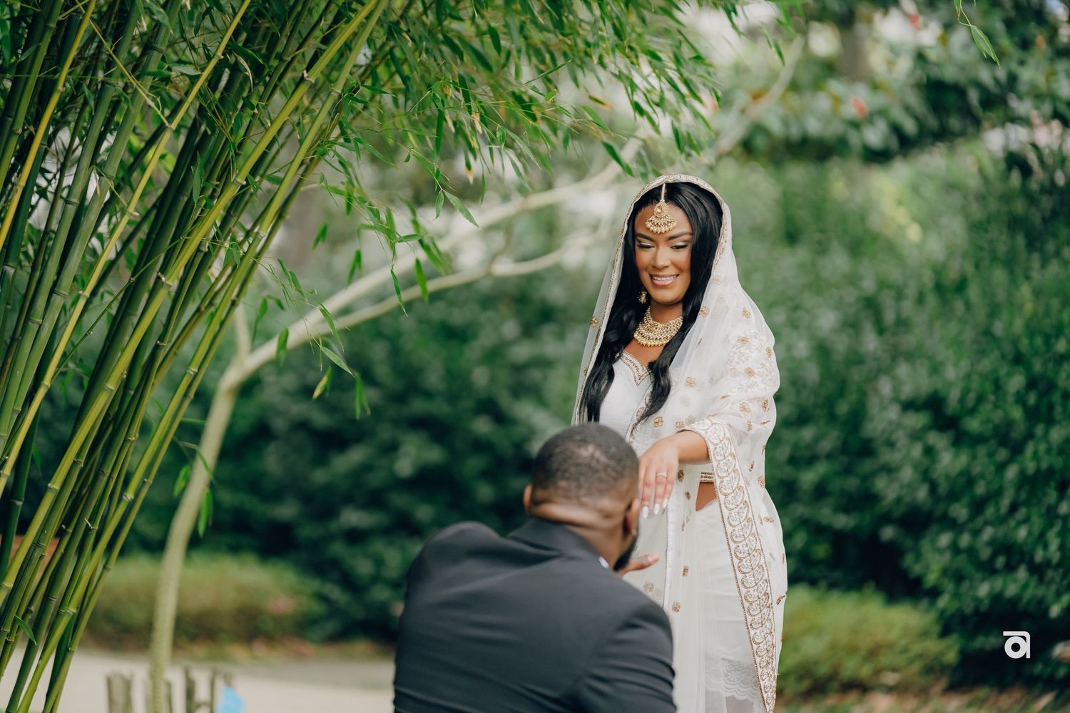 A romantic proposal scene in a lush garden setting with bamboo plants and greenery in the background.