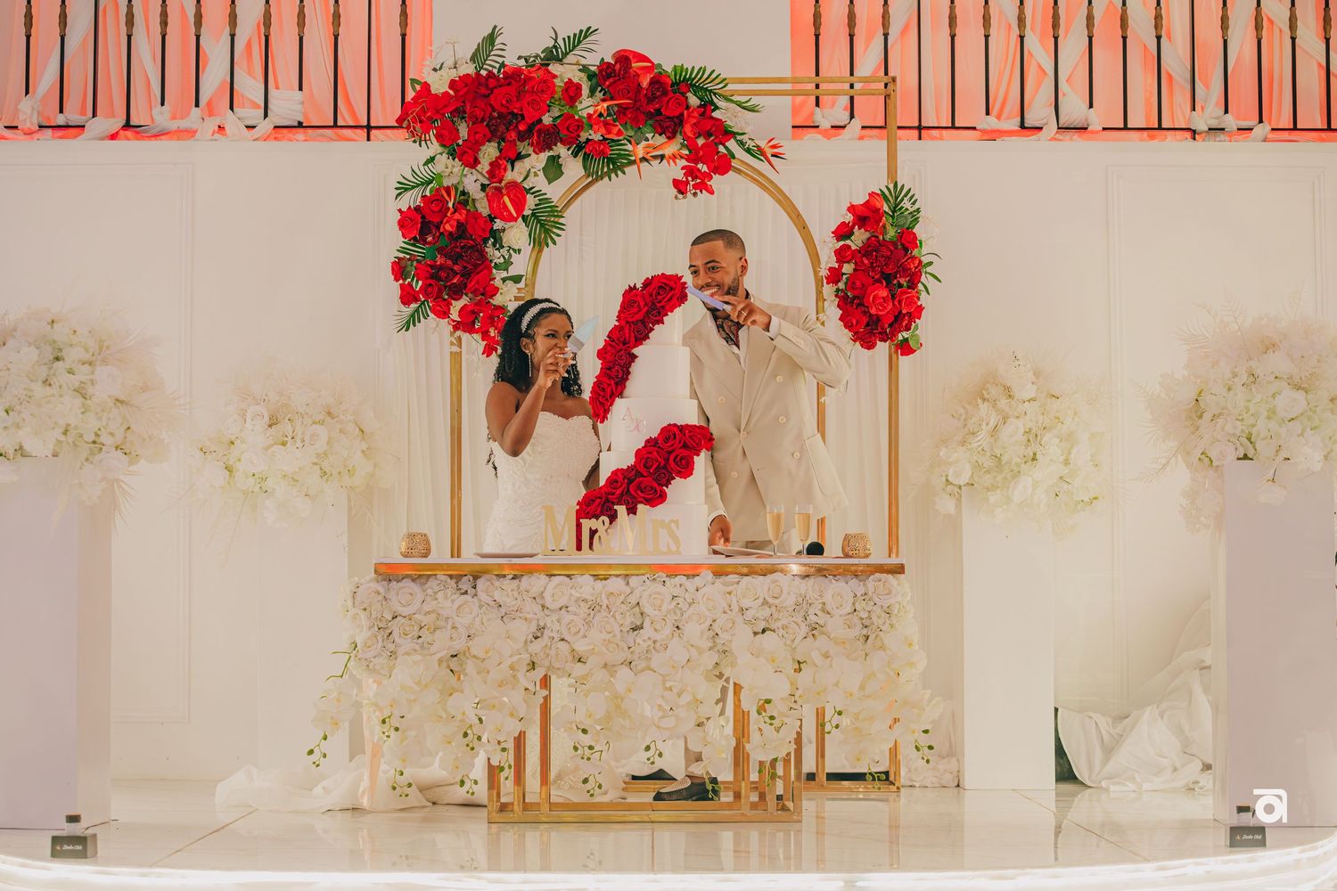 A beautifully decorated wedding arch with red roses and flowers frames a couples special moment at an elegant venue.