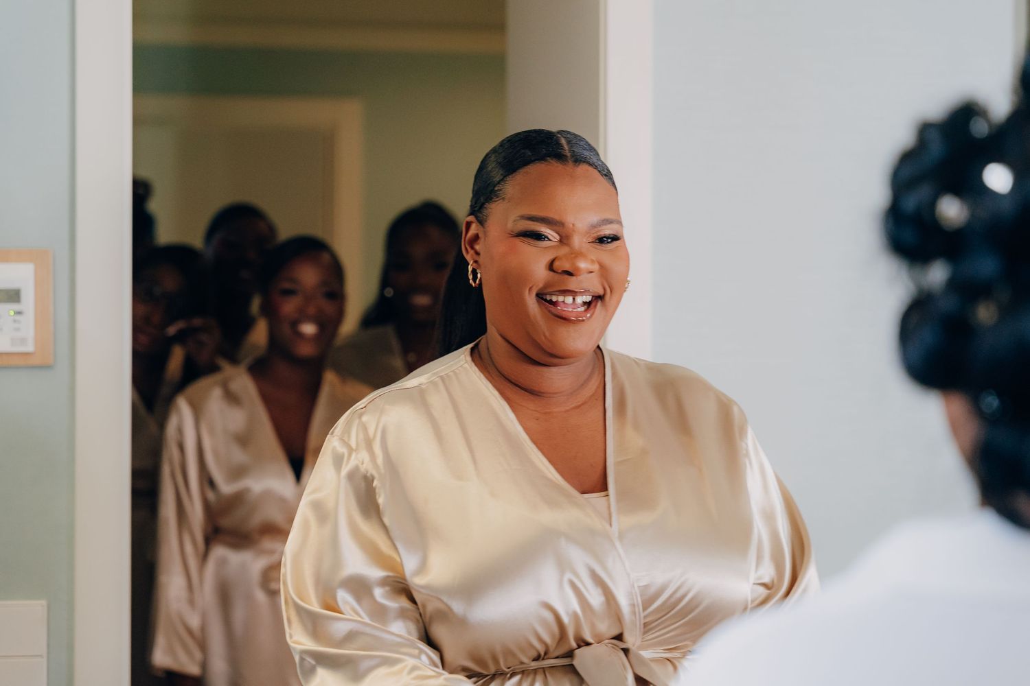 A person wearing a cream-colored satin wrap dress smiles joyfully during a special occasion celebration.