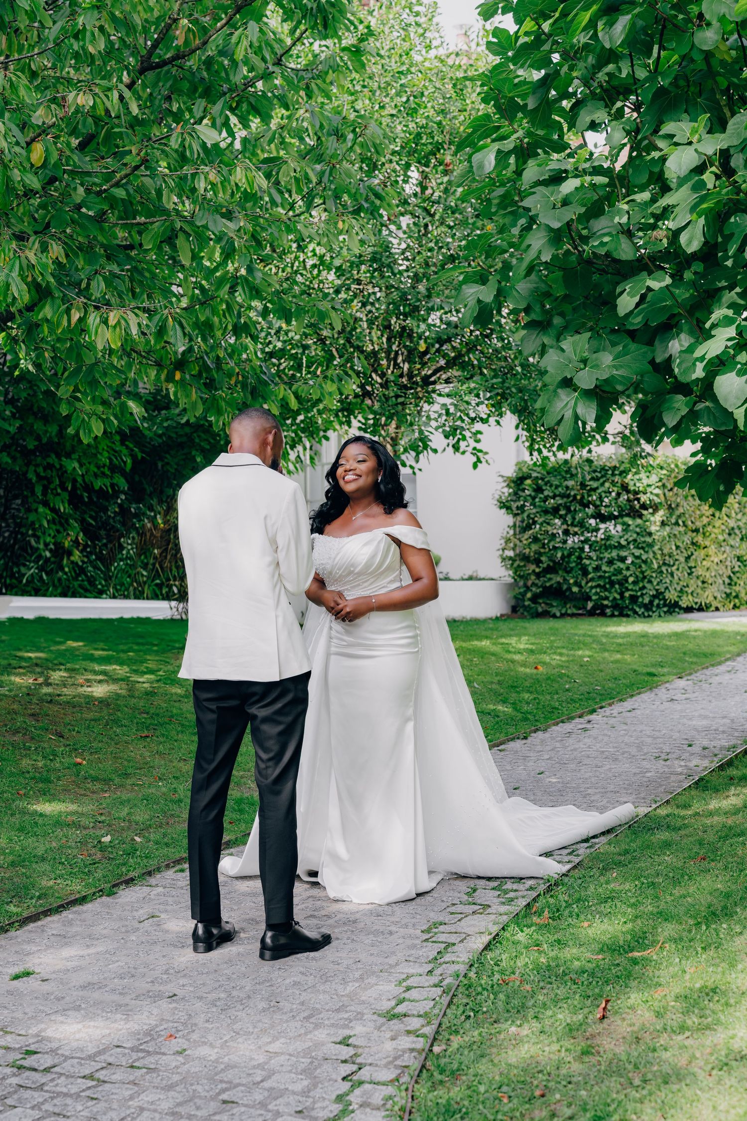 A couple walking along a garden path surrounded by lush greenery, with the bride wearing a flowing white dress.