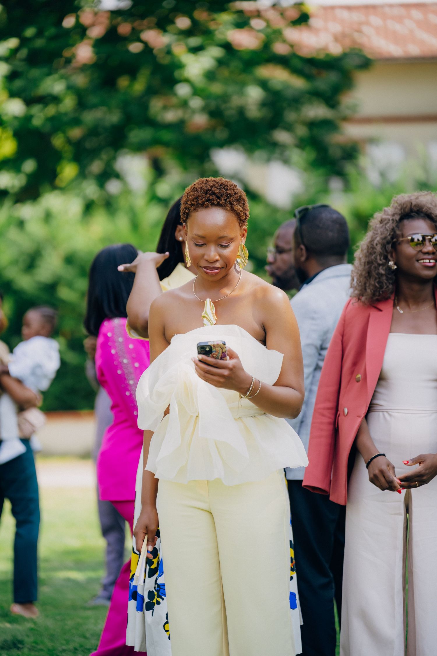 Wedding guests in bright formal attire gather outdoors for a celebration.