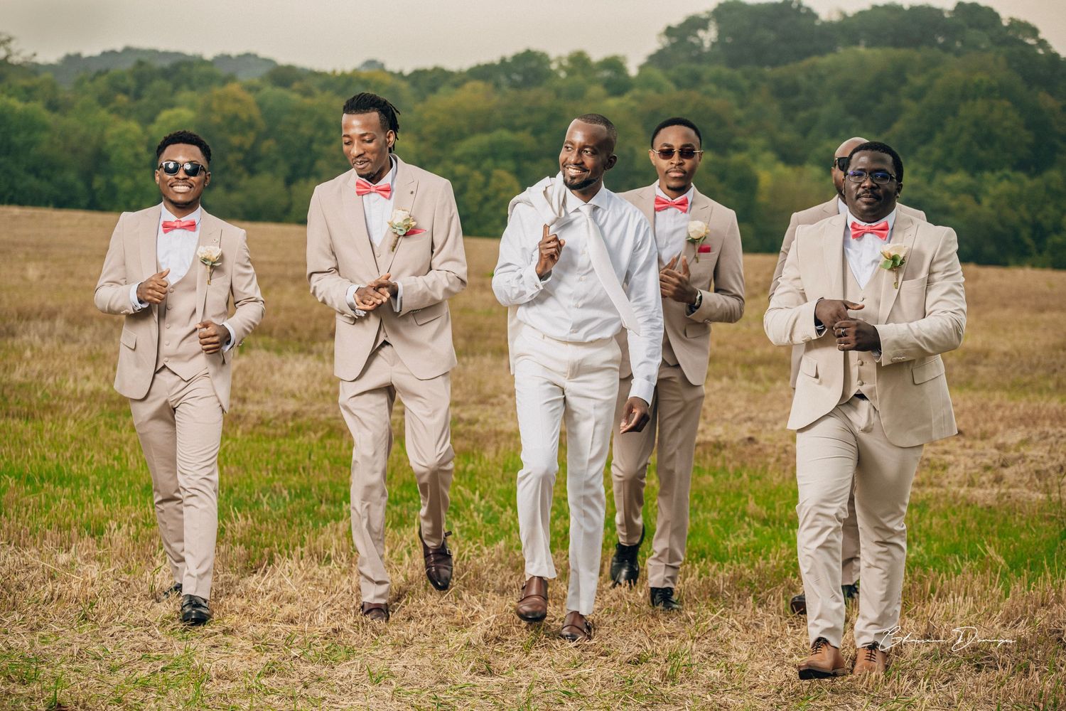 Groomsmen in beige suits walking together across a natural field setting.