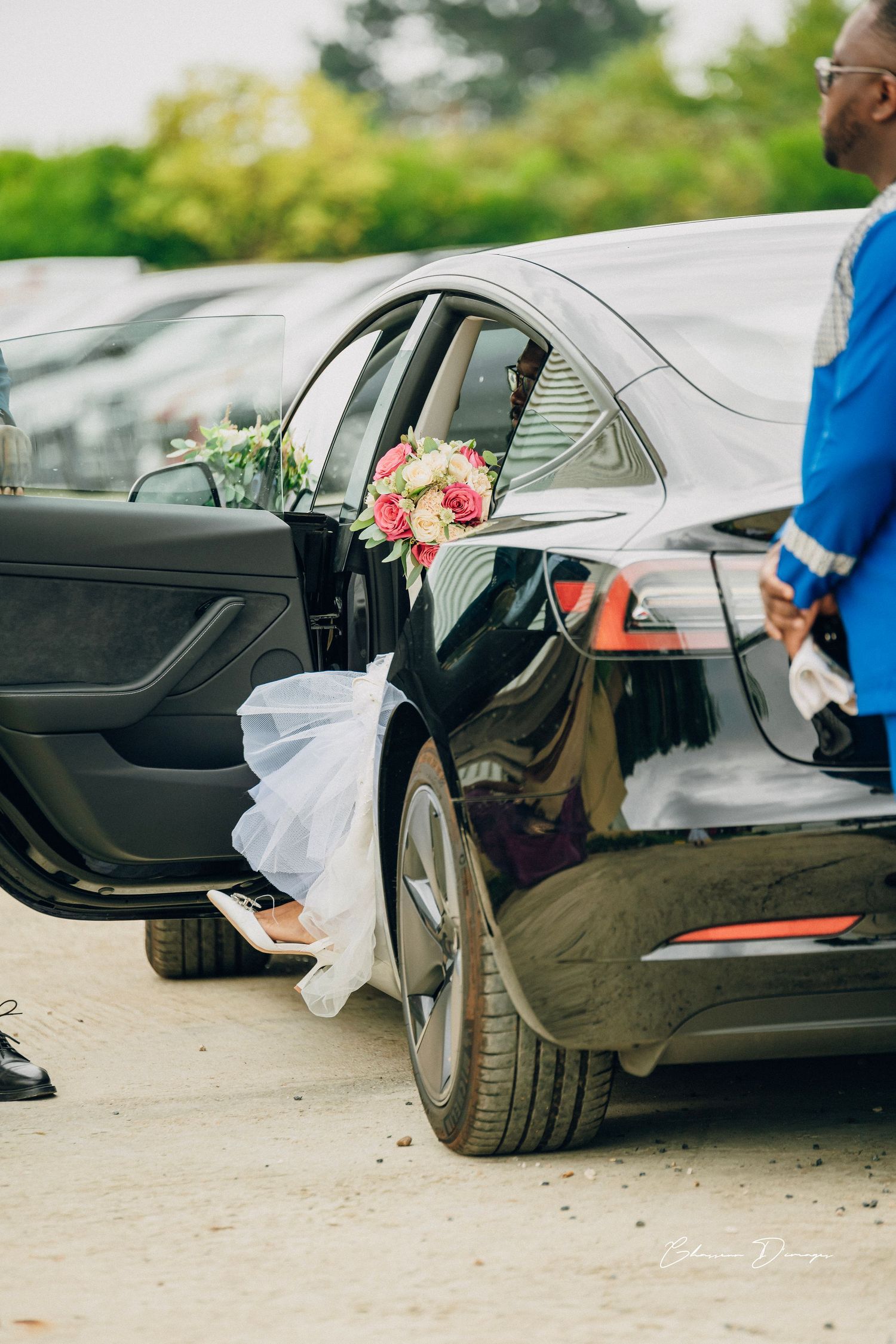 Decorated wedding car with floral arrangements and white tulle tied to the door.