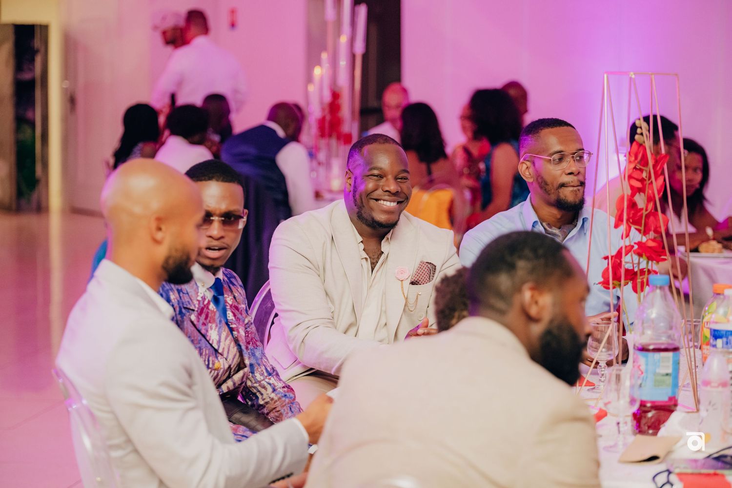 People enjoying conversation and laughter at a dinner table with pink lighting in the background.