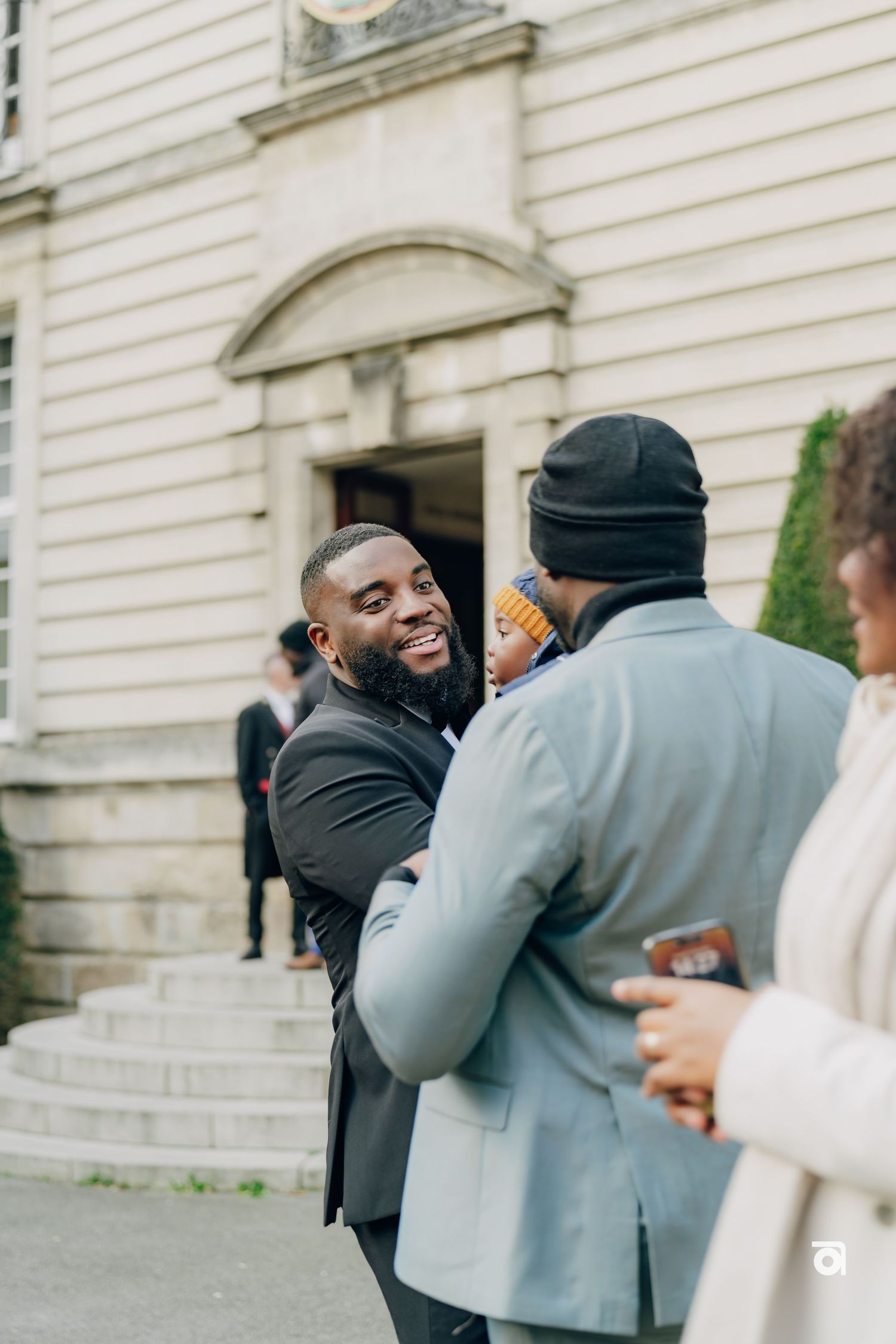 Two friends share a warm greeting and laugh outside a building with white siding and stone steps.