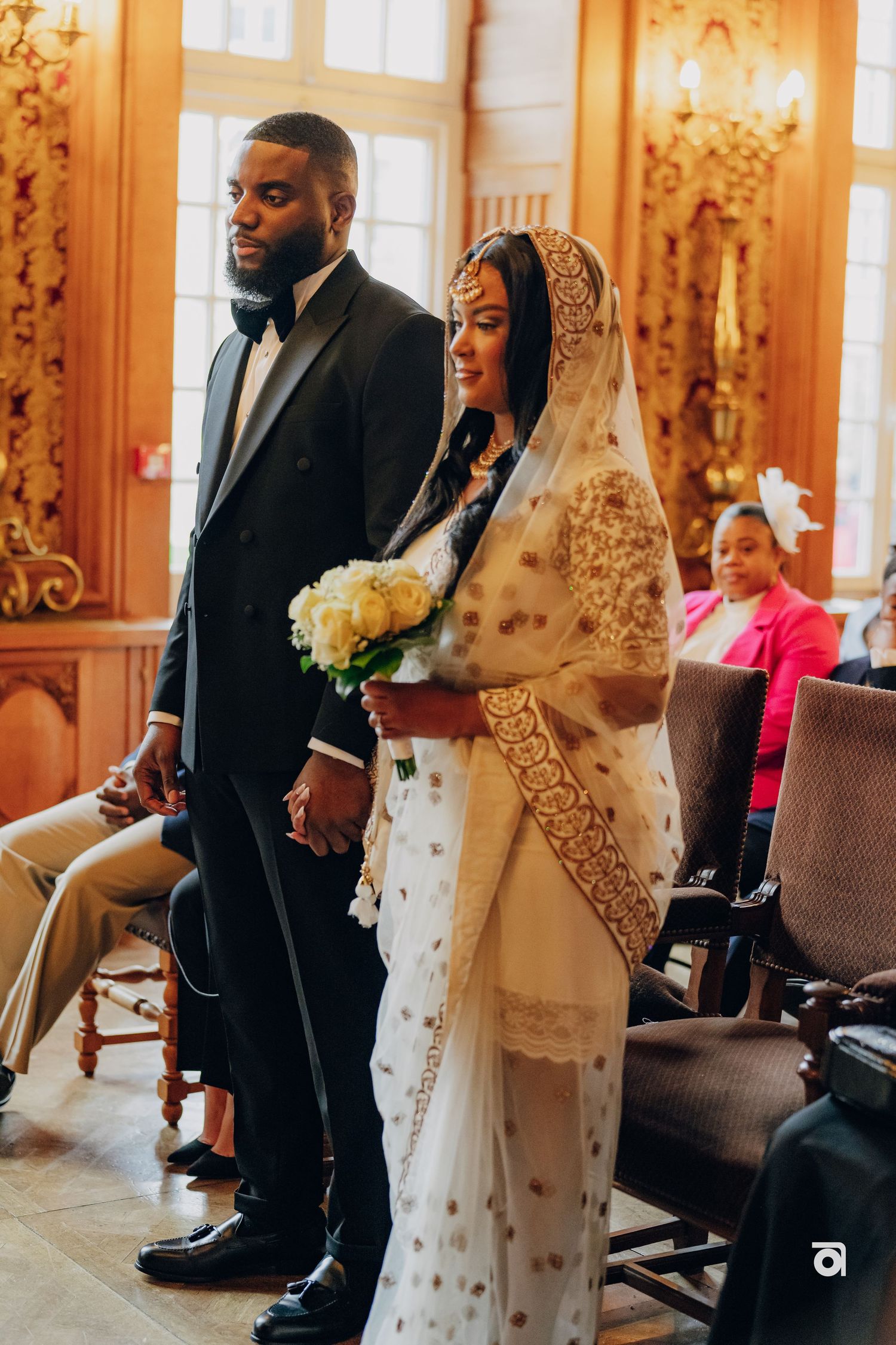 A couple stands together during their wedding ceremony in an ornate room with golden decor.