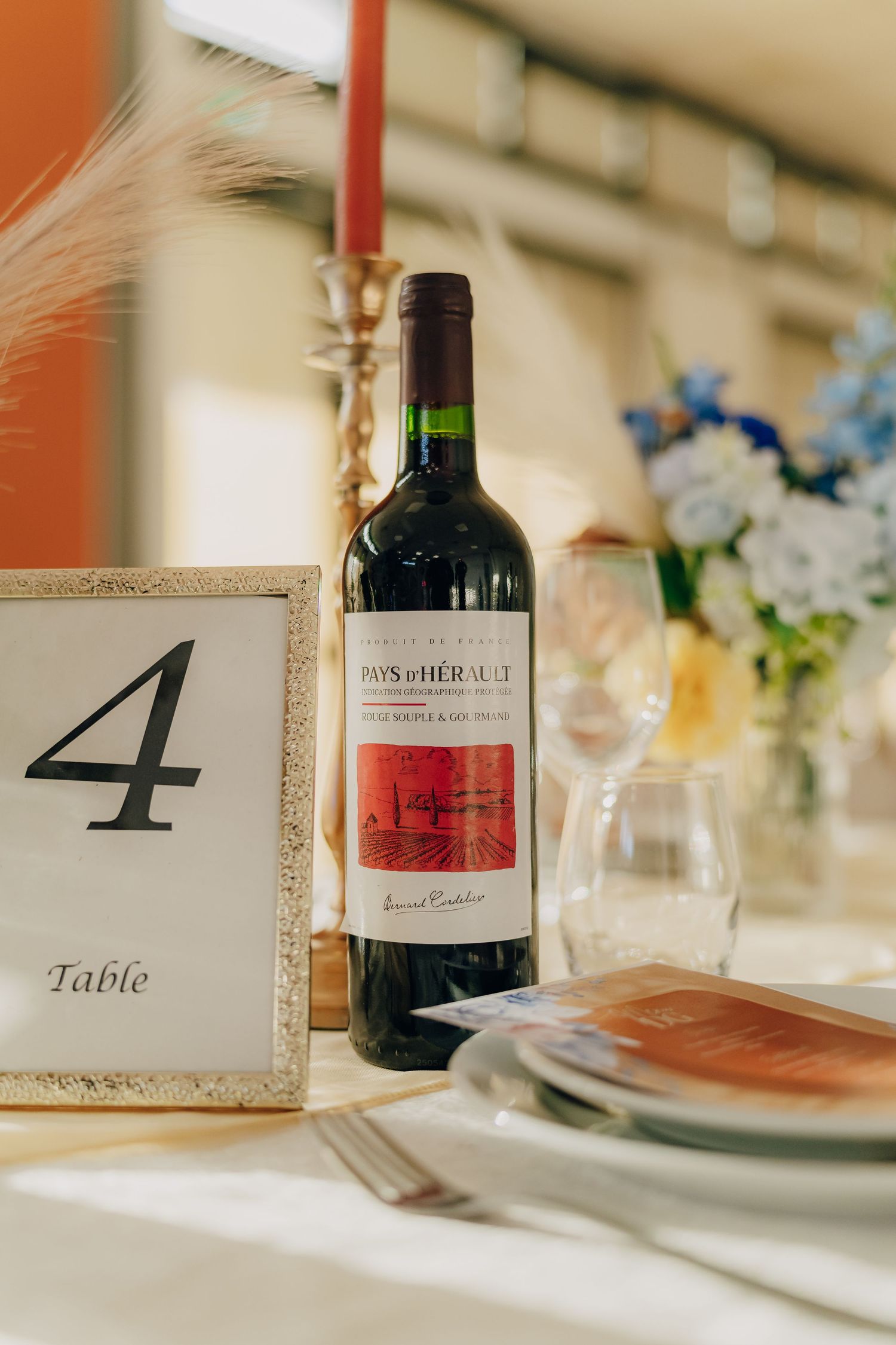 Wedding table setting with wine bottle, table number four, and white floral centerpiece arrangement.