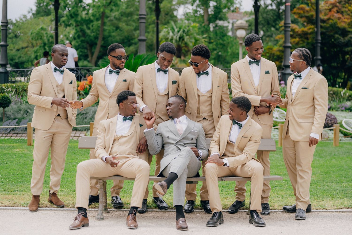 Groomsmen in tan suits sit casually on steps during outdoor wedding photo session.