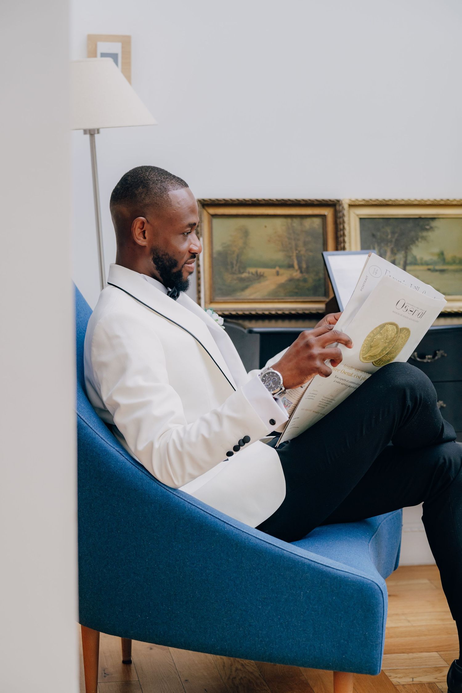 A person in a white blazer reclines in a blue armchair while reading a document.