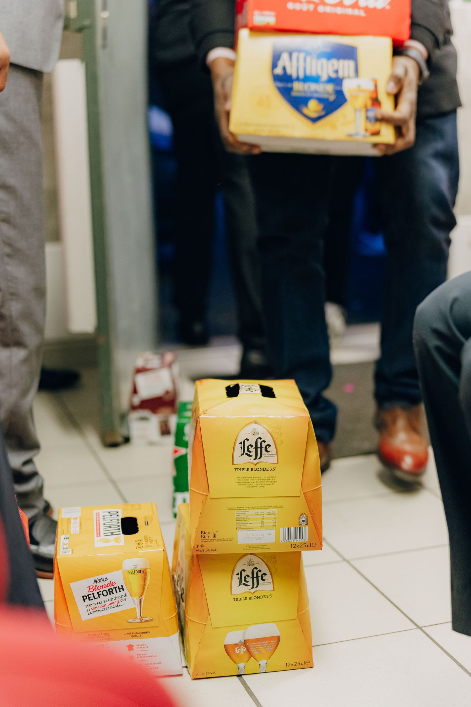 Boxes of Leffe and Affligem beer stacked on white tile floor.