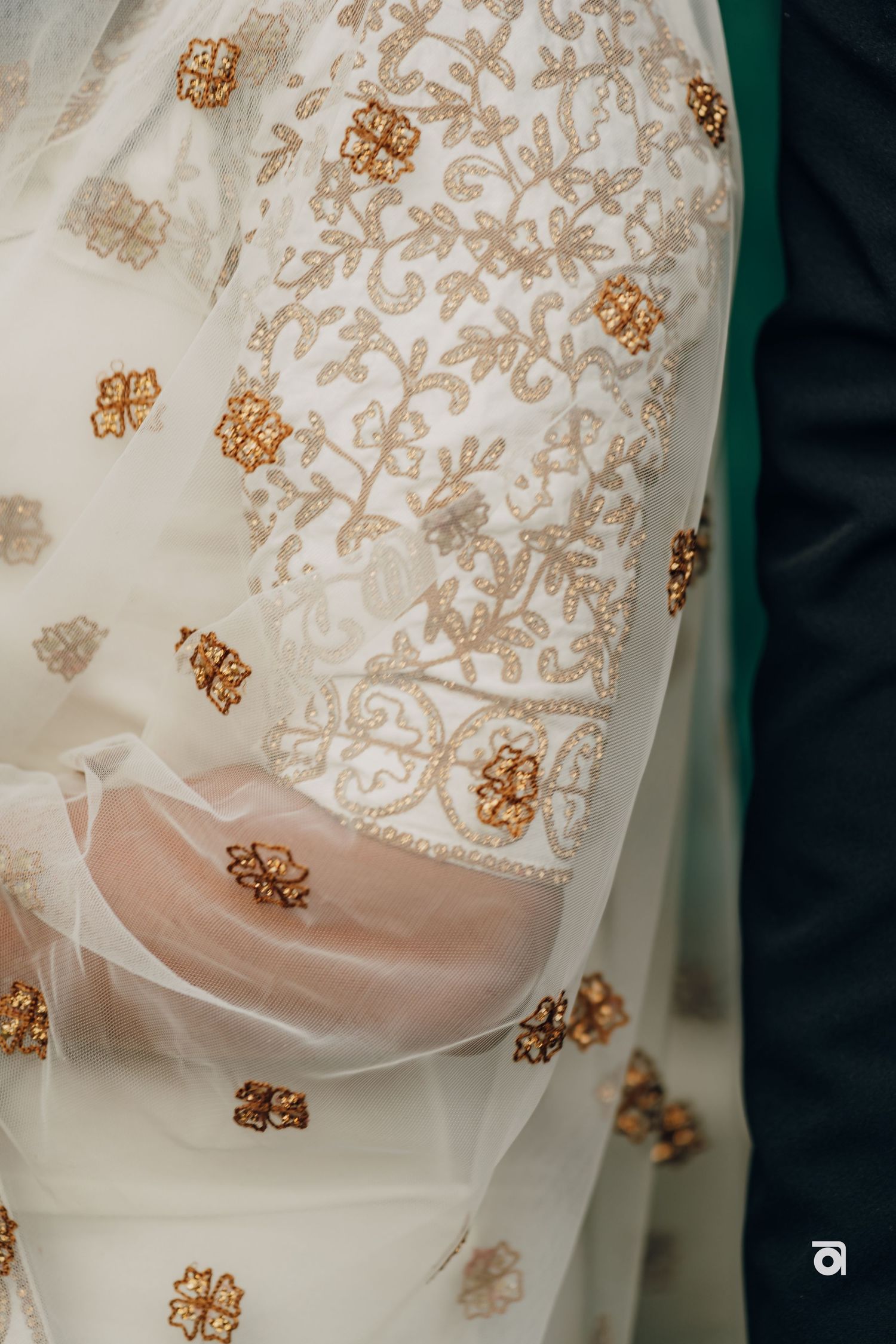 Close-up detail of intricate gold floral embroidery on white wedding dress fabric.