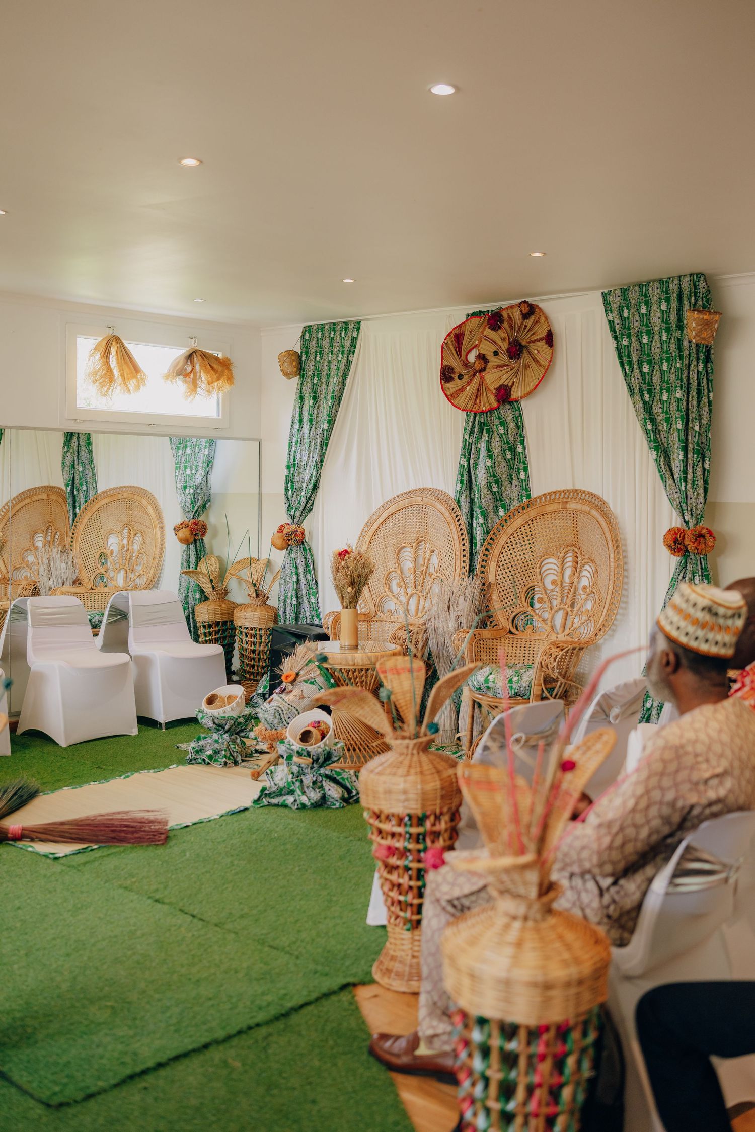 Traditional wedding decor setup with green carpet, white chairs and ornate gold accents in an indoor venue.