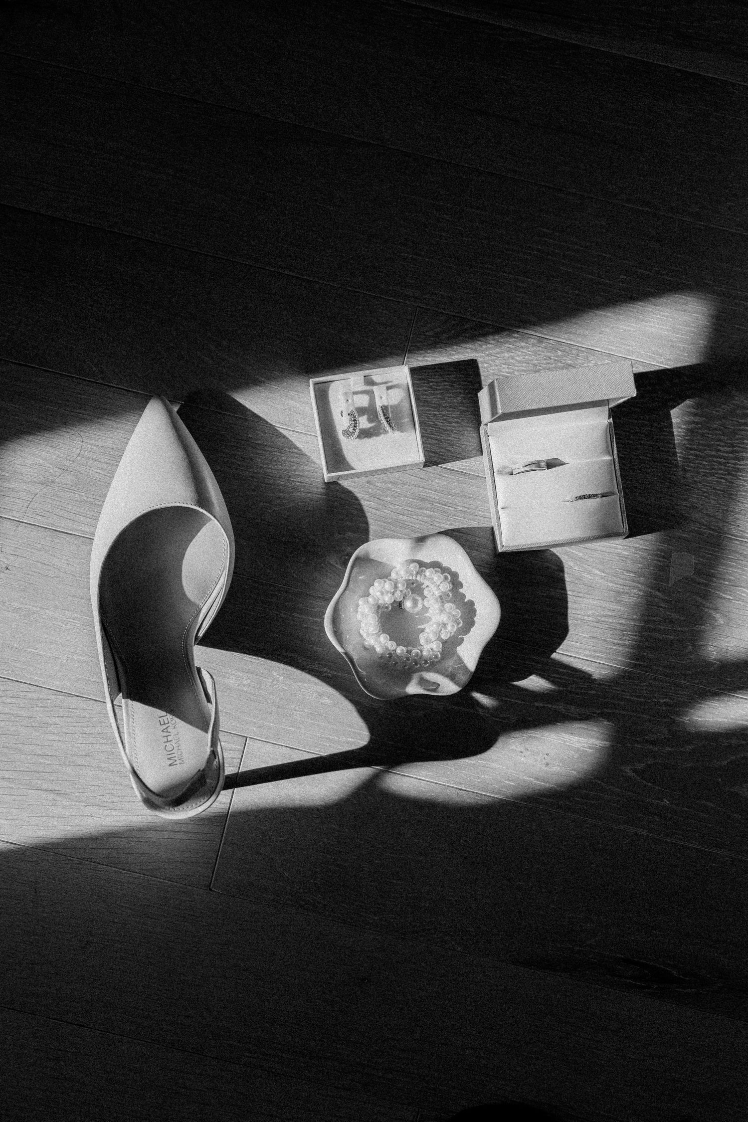 Black and white photo of a high heel shoe and small objects casting dramatic shadows on a wooden floor.