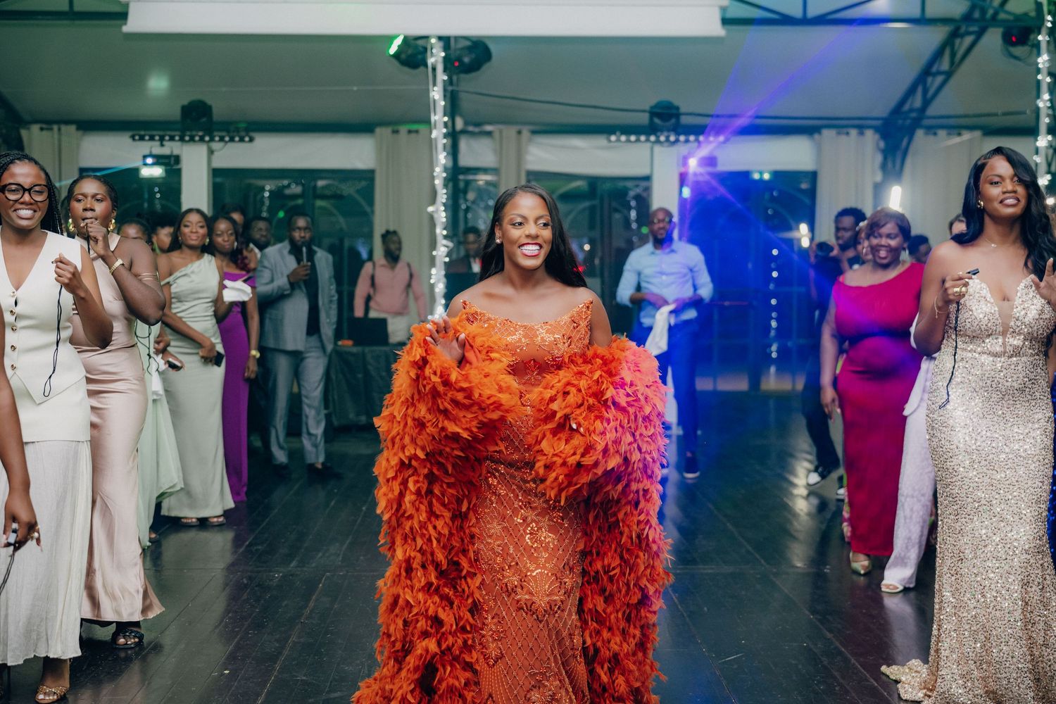 Wedding guest in a stunning orange feathered gown makes a grand entrance on the dance floor.