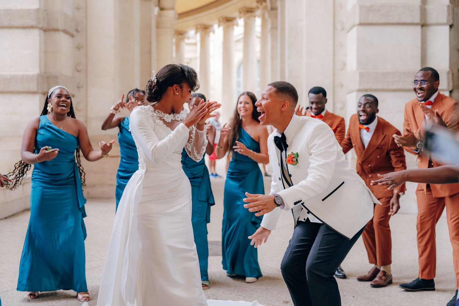 Wedding party in teal blue dresses and coral suits dancing in a line during reception celebration.