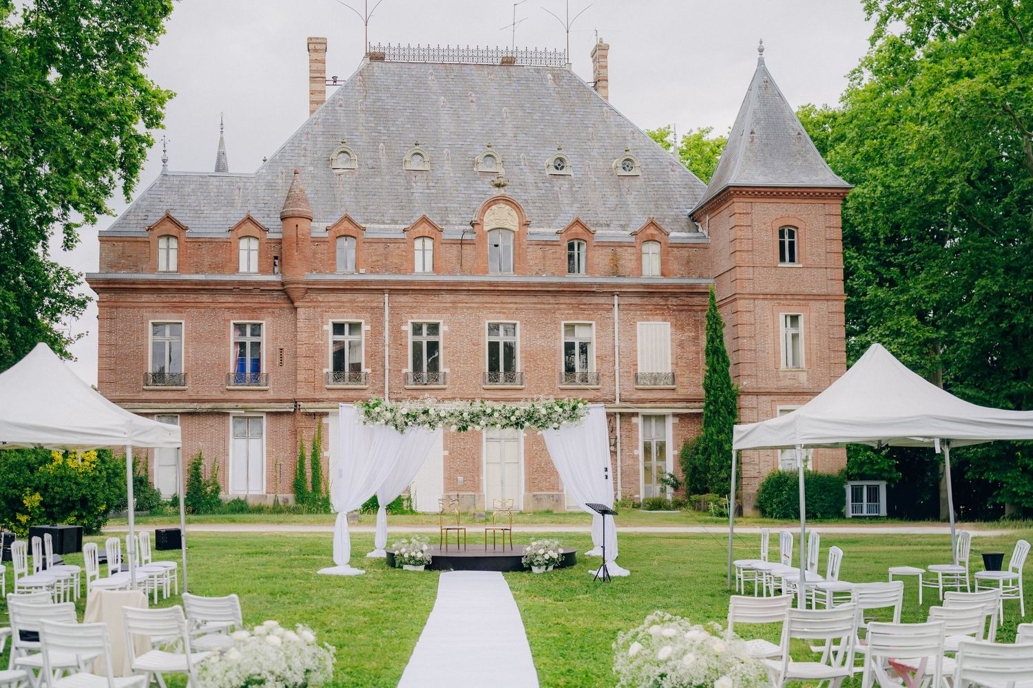 A rustic chateau wedding venue with elegant outdoor ceremony setup featuring white chairs and floral decorations.