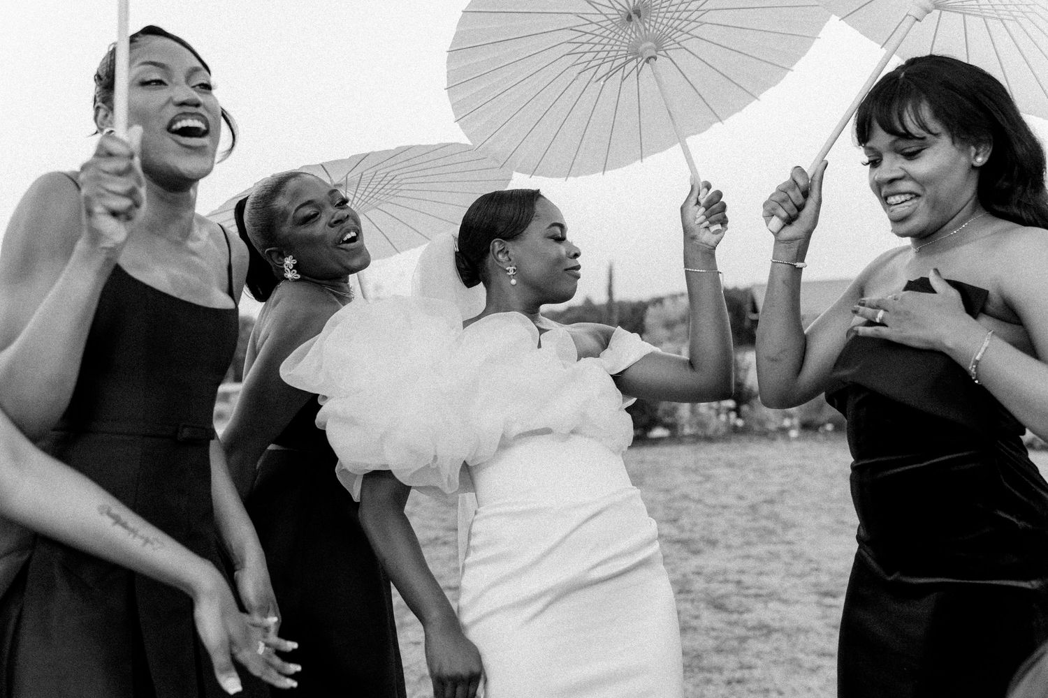 A collection of joyful wedding party photos in black and white showing people laughing and holding white parasols.