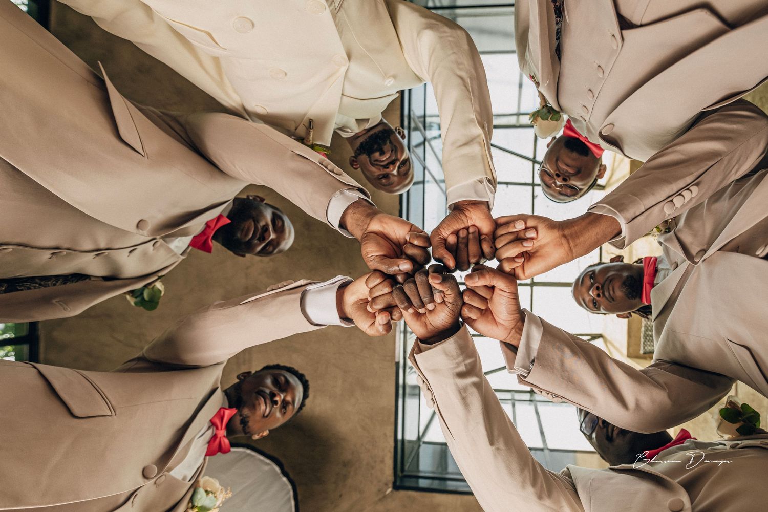Overhead view of groomsmen joining hands in circle wearing matching beige suits.