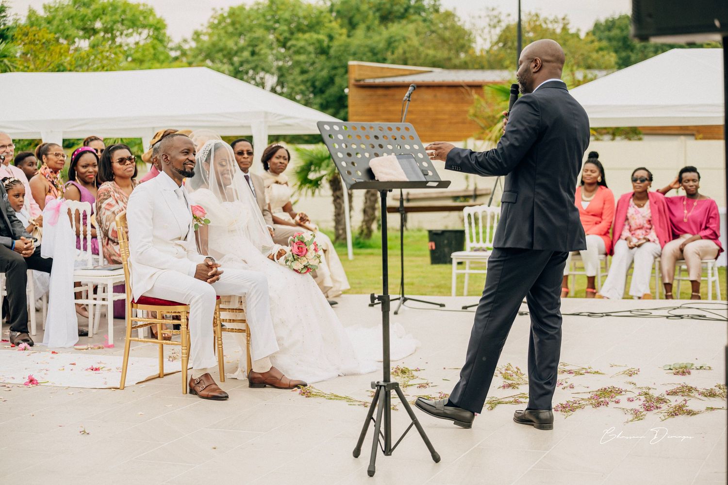 Officiant conducts wedding ceremony with couple seated outdoors.