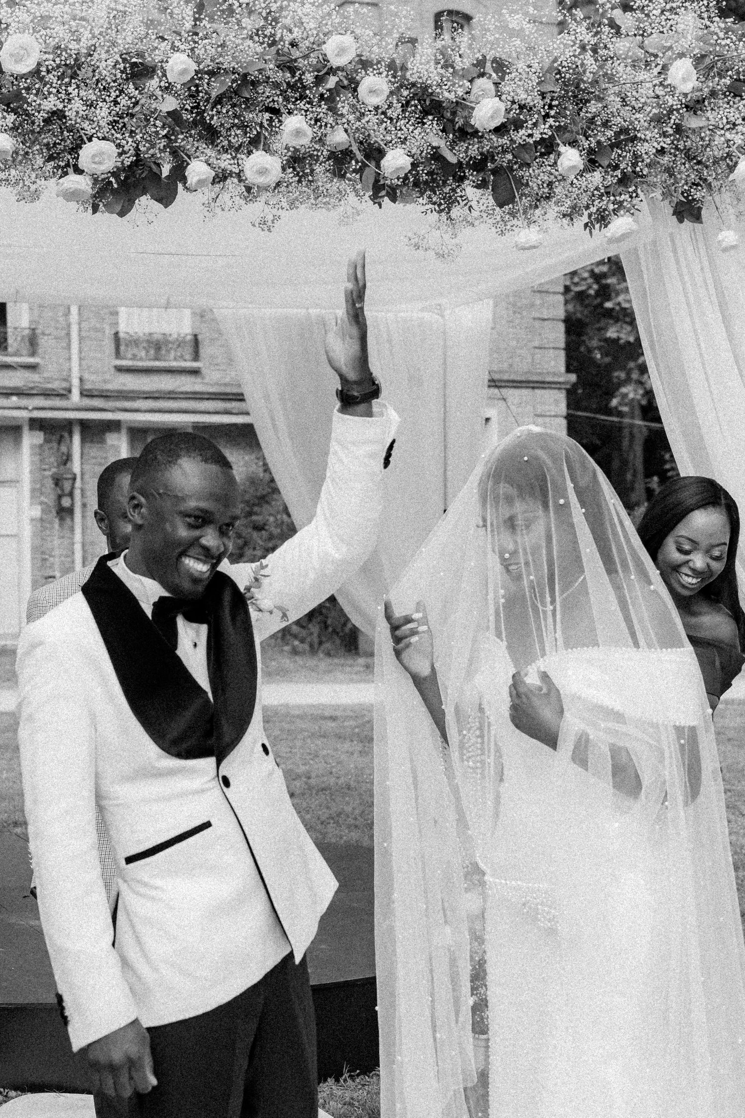 Black and white photo of wedding party members celebrating behind sheer white curtains.