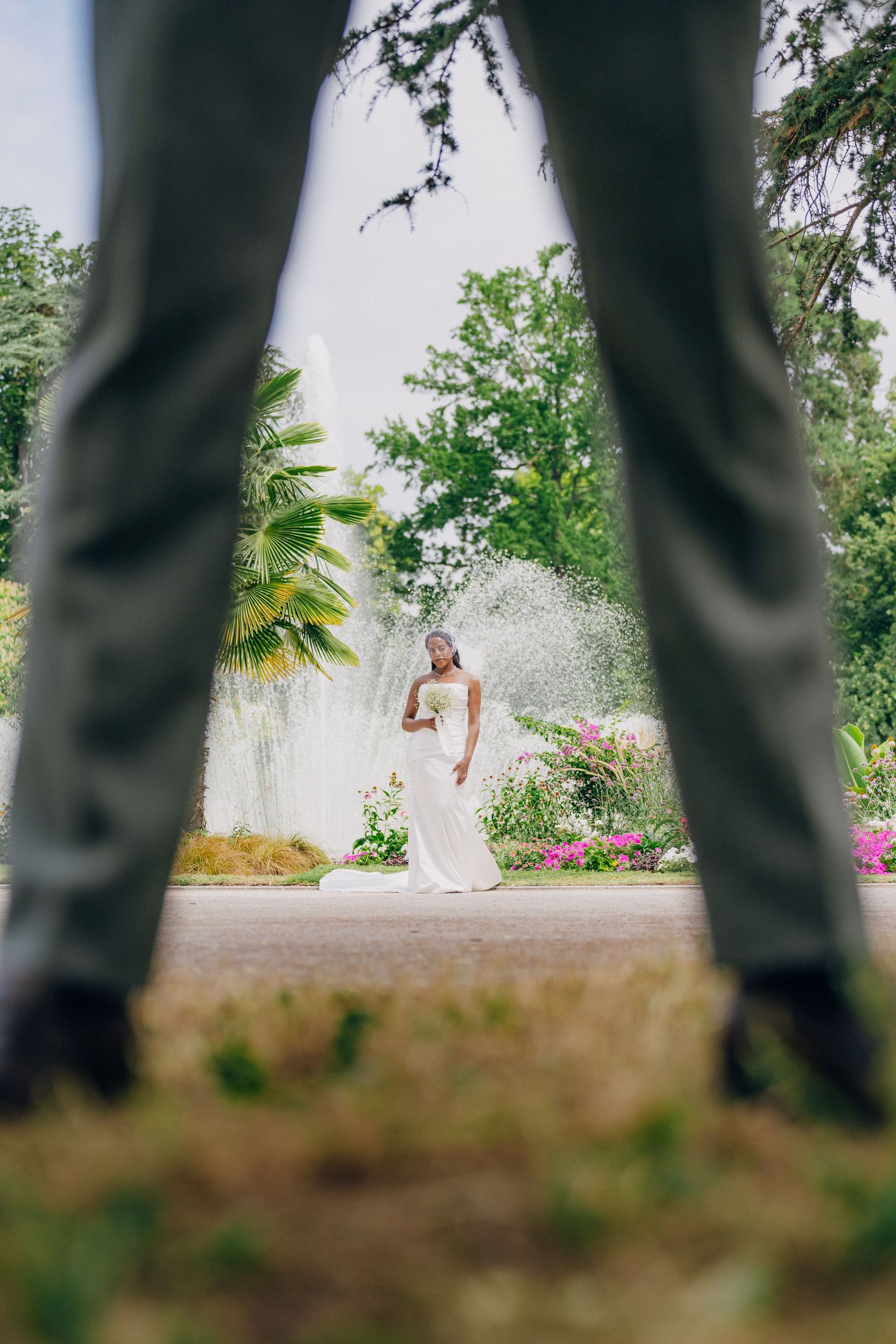 Artistic wedding photo composition showing a bride through dark tree trunks in a garden setting.