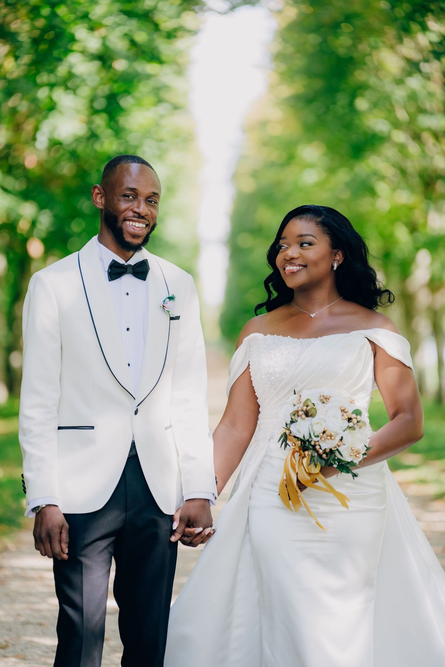 Joyful wedding couple poses together outdoors in a wooded setting with natural greenery in the background.