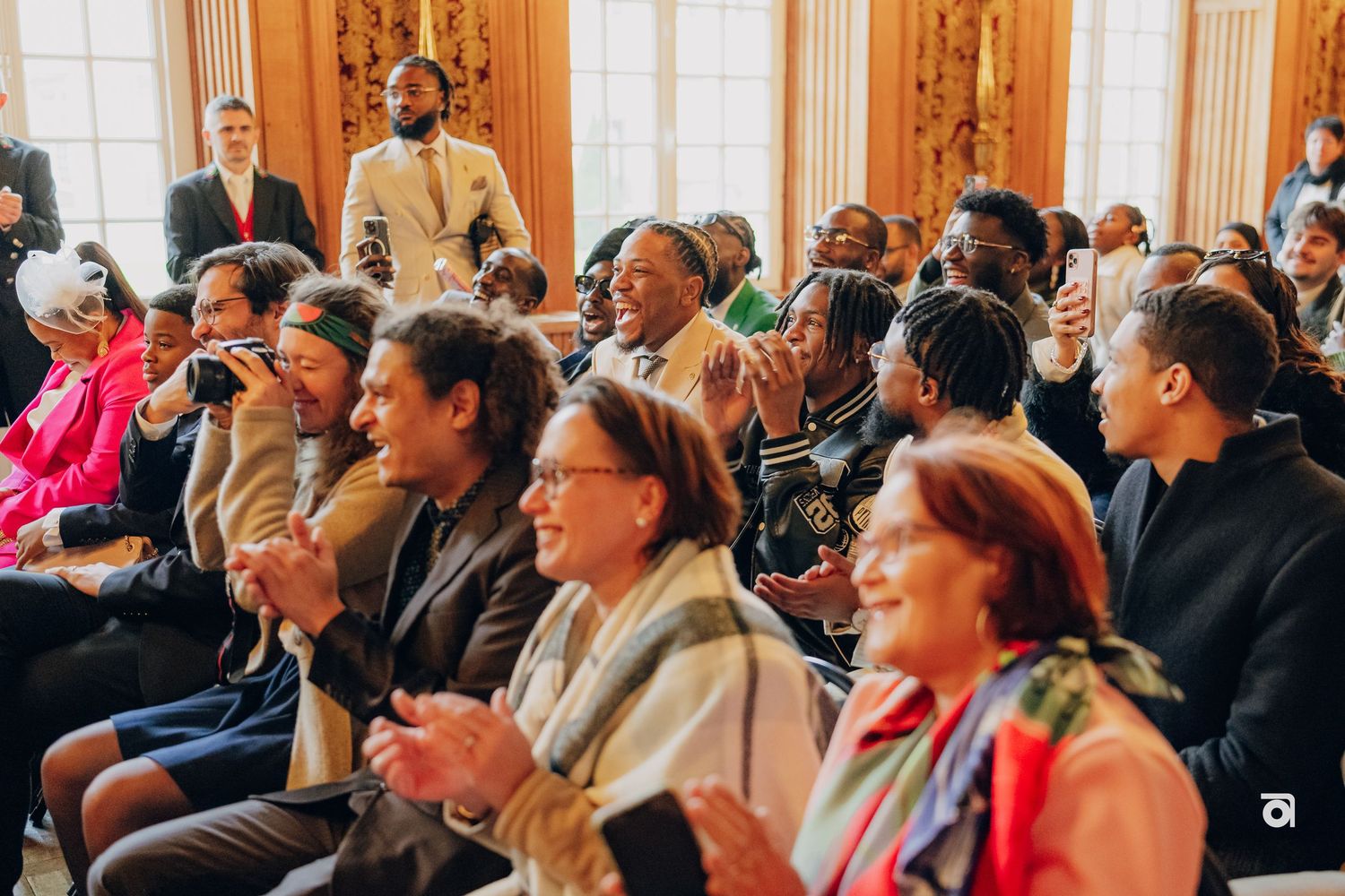Diverse wedding guests seated in ornate venue reacting with joy.