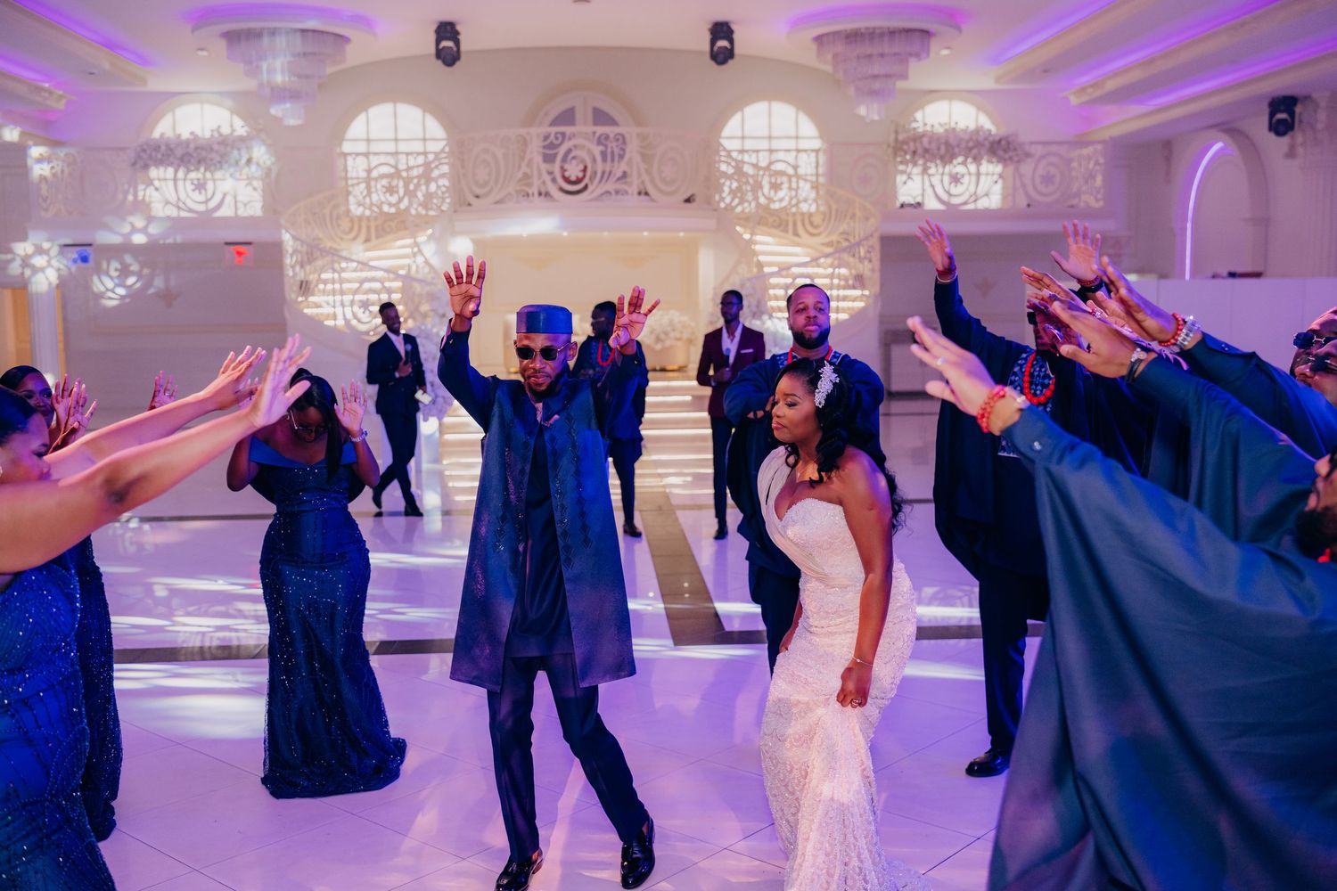 Wedding celebration with guests dancing and raising hands on a glowing purple-lit dance floor.