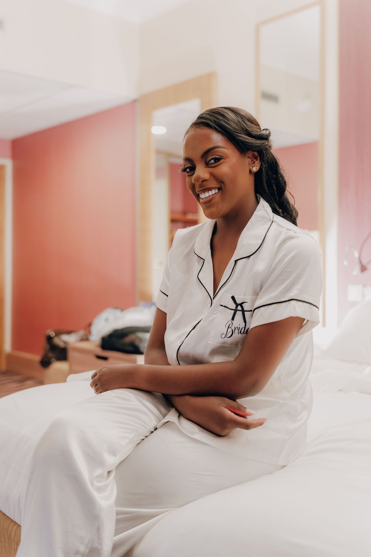 A person in white sleepwear lounges comfortably on crisp white bedding in a room with coral-colored walls.