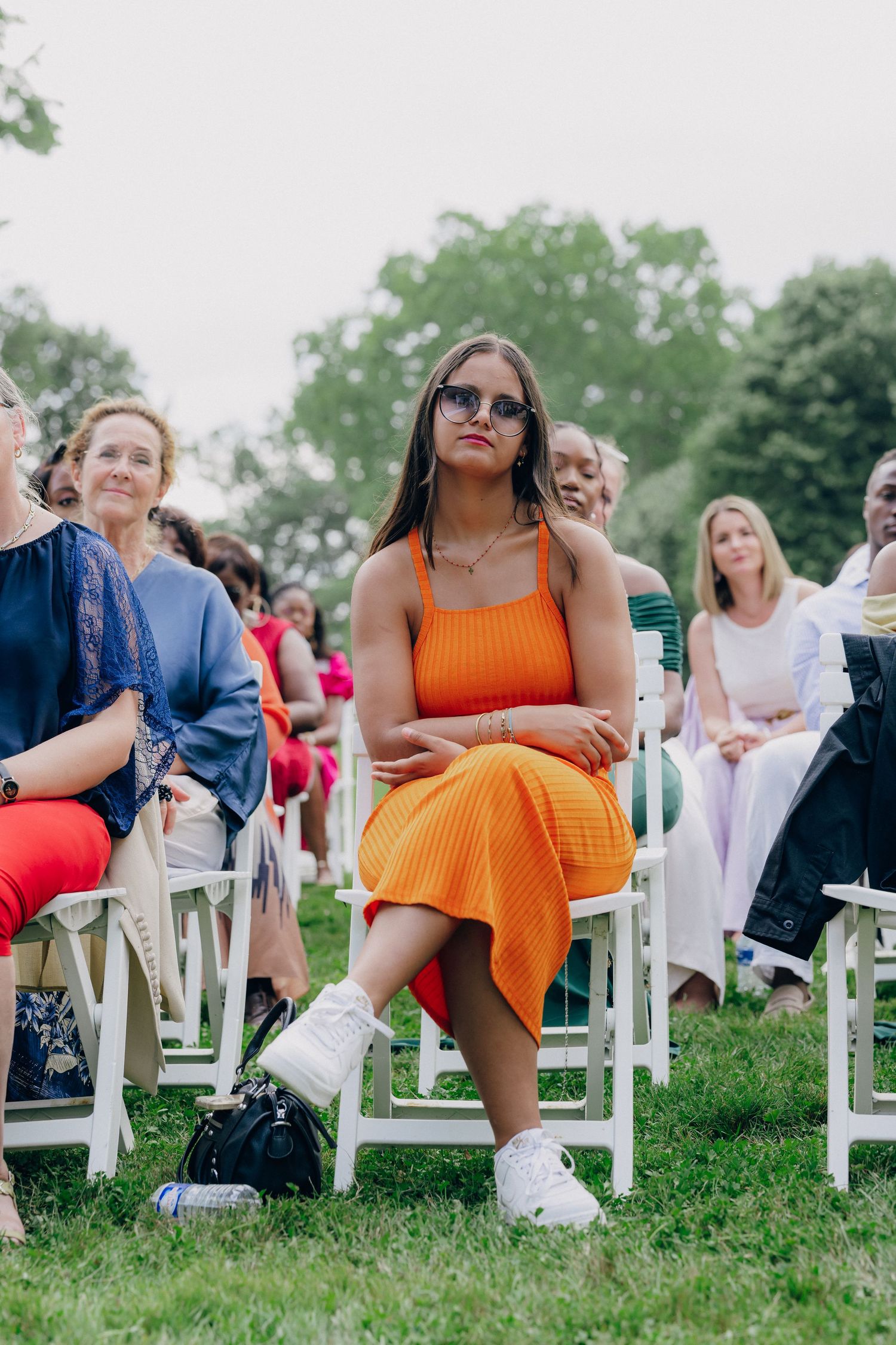 Wedding guests sit in white chairs on a grassy lawn during an outdoor ceremony.
