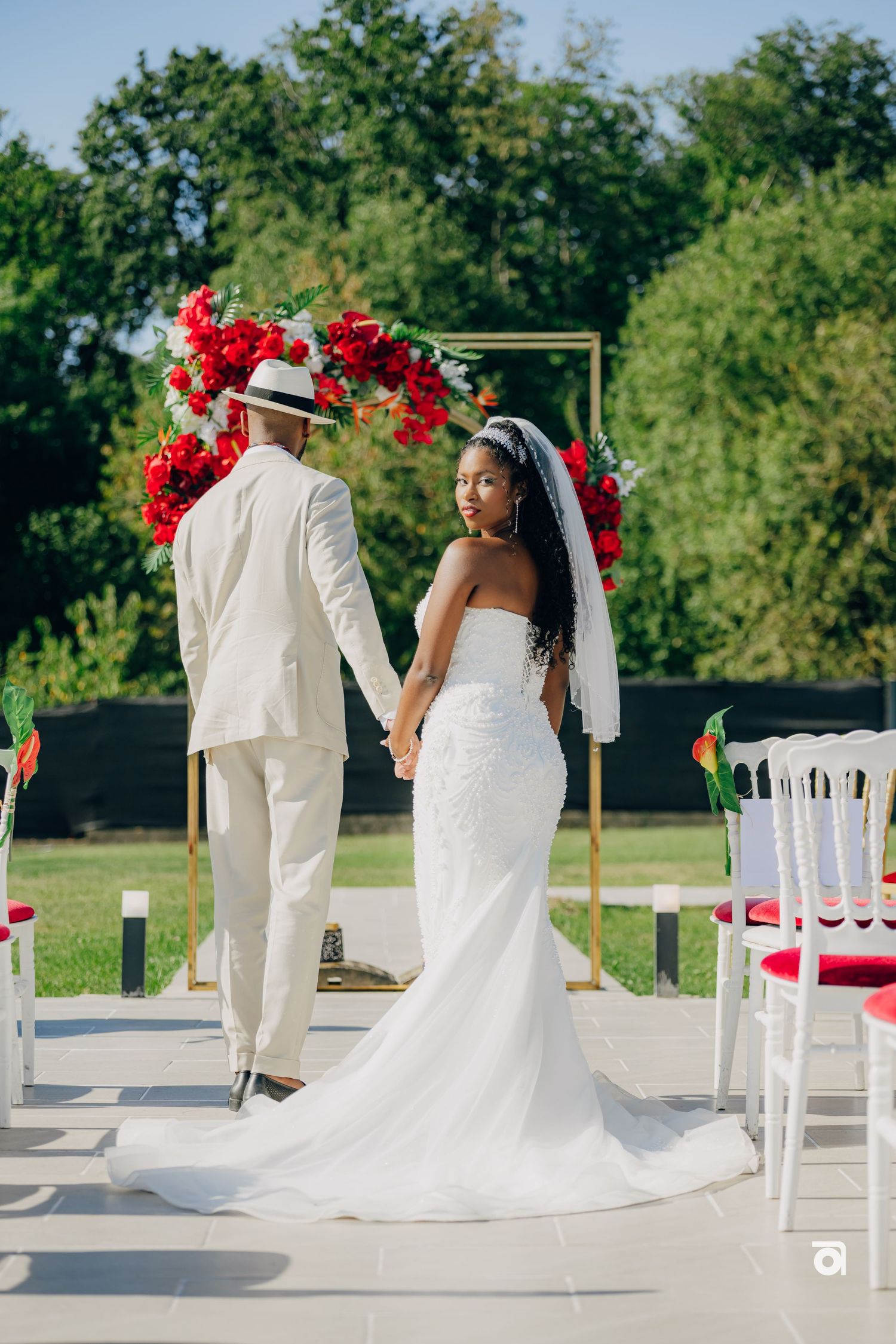 A newly wedded couple stands at a beautiful outdoor ceremony venue decorated with red floral arrangements and white chairs.