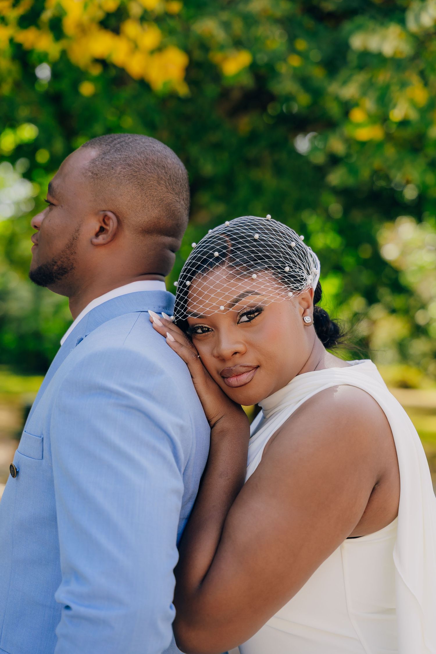 A romantic wedding couple embraces outdoors against a blurred green and yellow natural background.