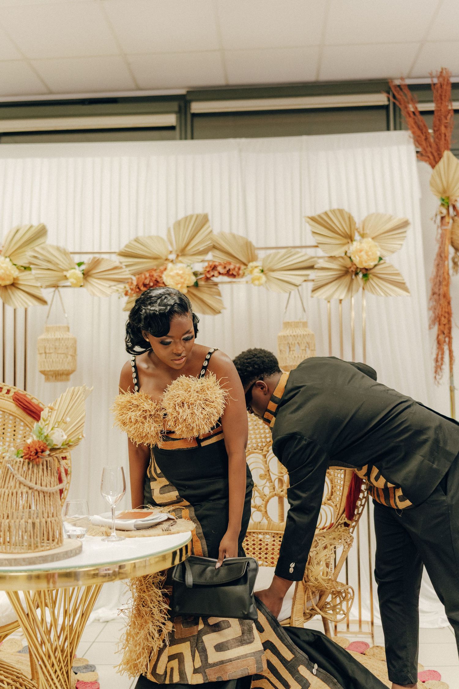 A couple stands near a decorative display with gold straw fans and festive decor.