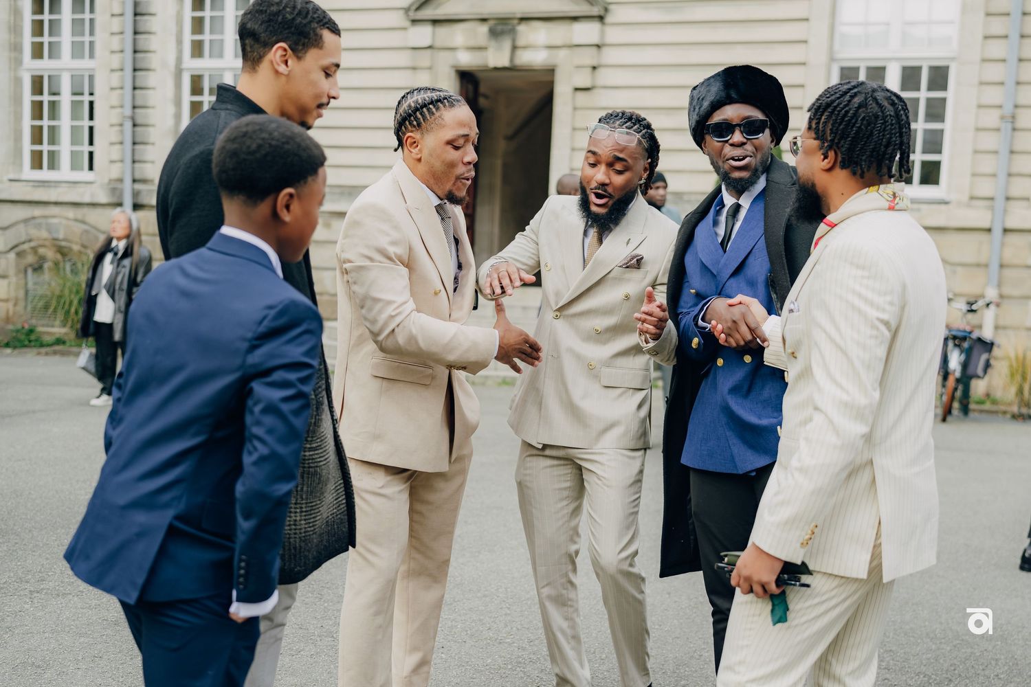 A group of well-dressed friends in suits share a lighthearted conversation together outside a building.
