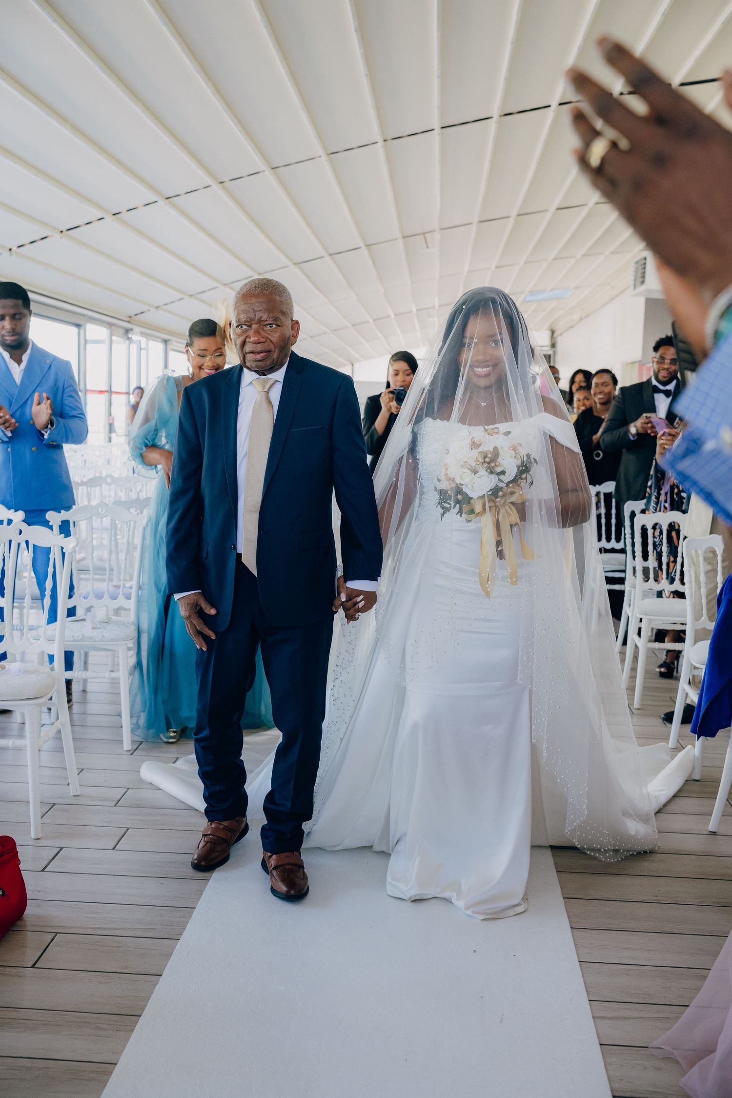 A wedding processional shows a bride in white walking down the aisle with floral decor overhead.