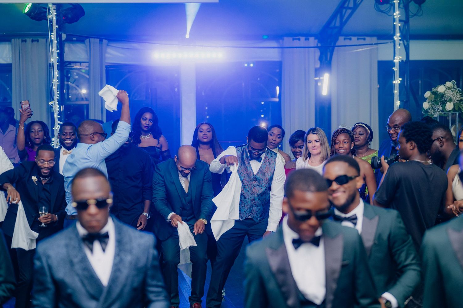 Formal event with guests in elegant attire dancing under blue lighting.