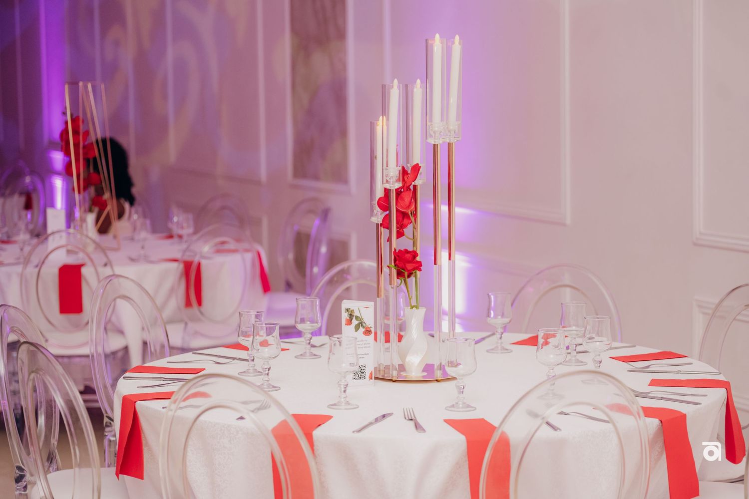 Elegant wedding reception table settings with tall white candles and coral accents in a white banquet hall.