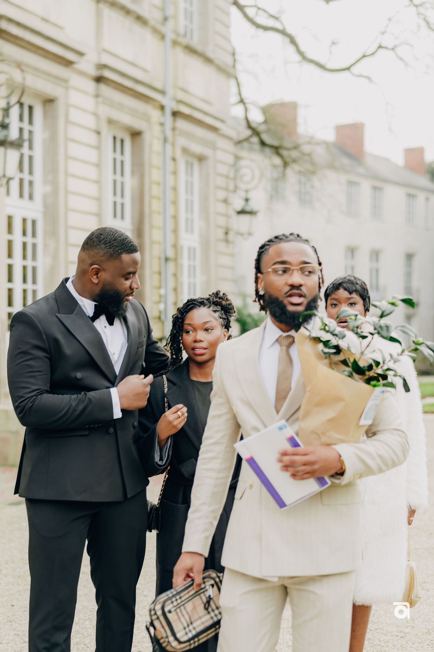 Wedding guests in formal attire gathering outside a classic French-style building.