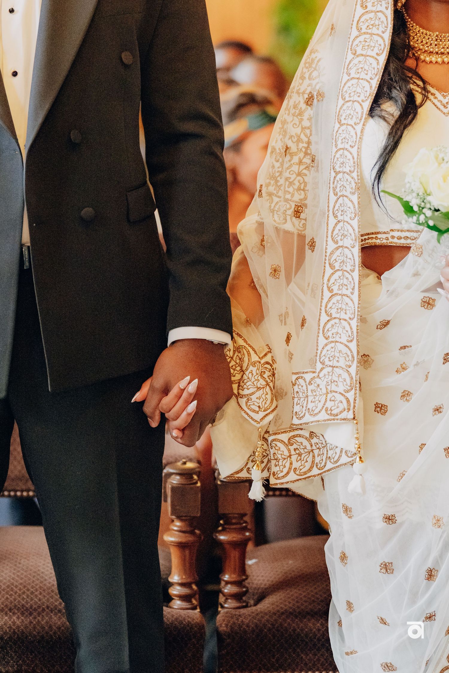 Close-up of couple holding hands, showing wedding attire detail with intricate white lace and black suit.