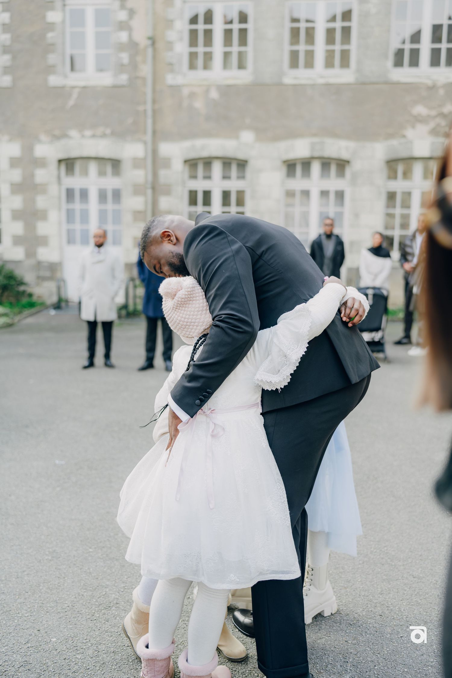 A tender moment between two people embracing at a formal event outside a grand building with large windows.