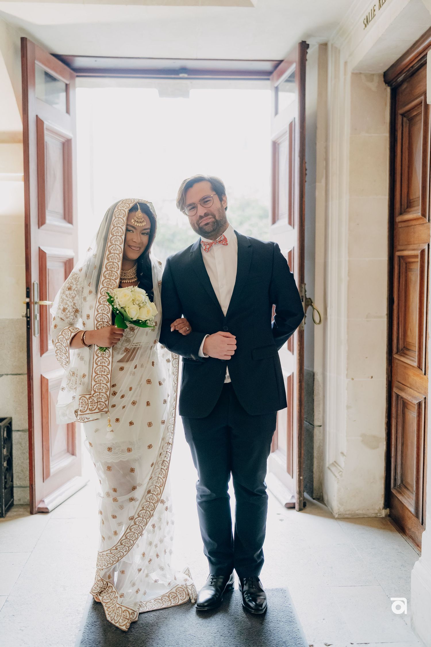 A couple in formal attire stands in a doorway during a traditional wedding ceremony.