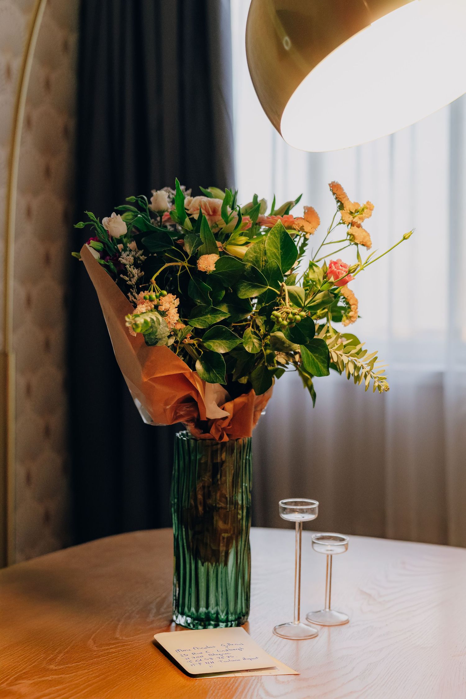 A series of elegant floral arrangements in glass vases sit on a wooden table with soft lighting and curtains in background.