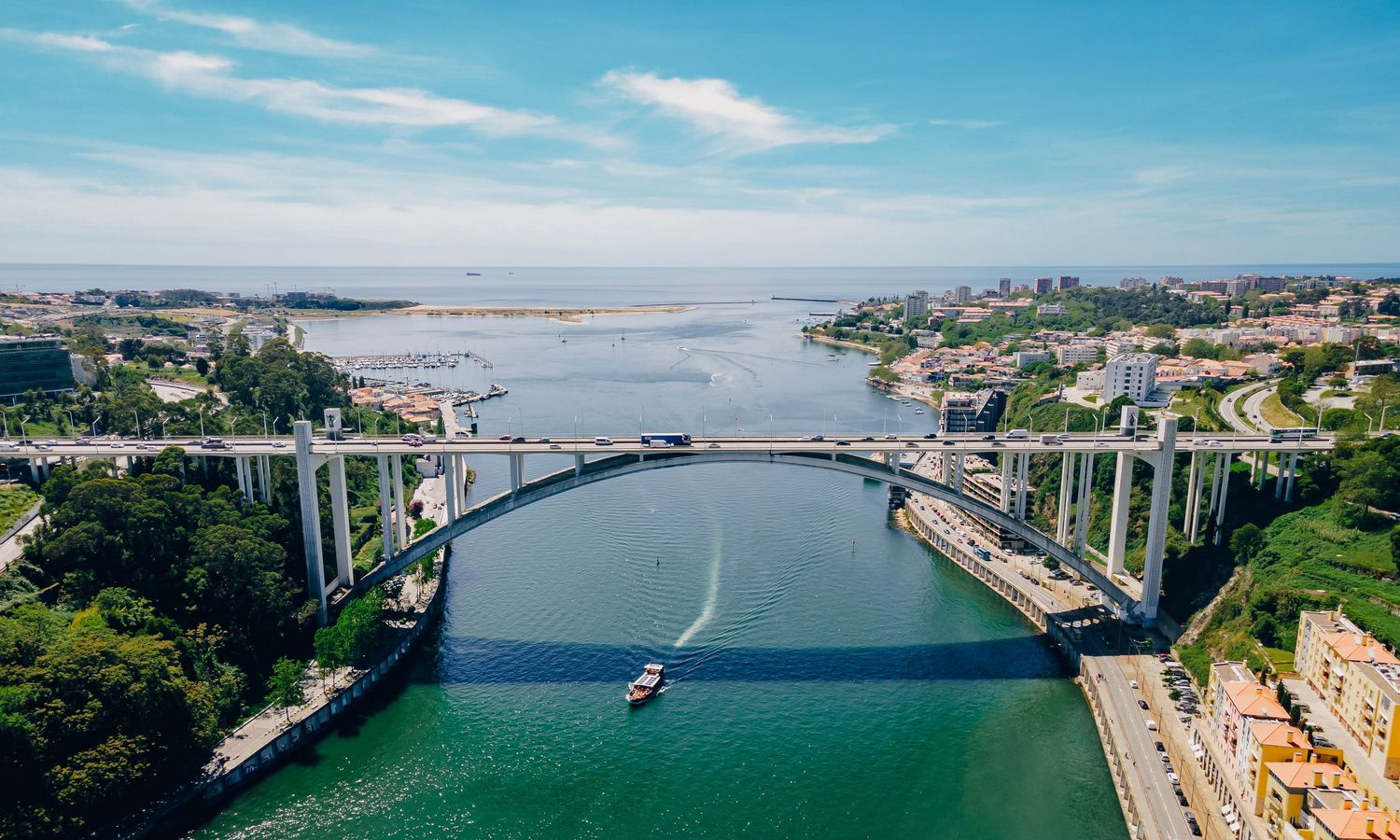 Bridge spanning waterway between green coastal cities under blue sky.