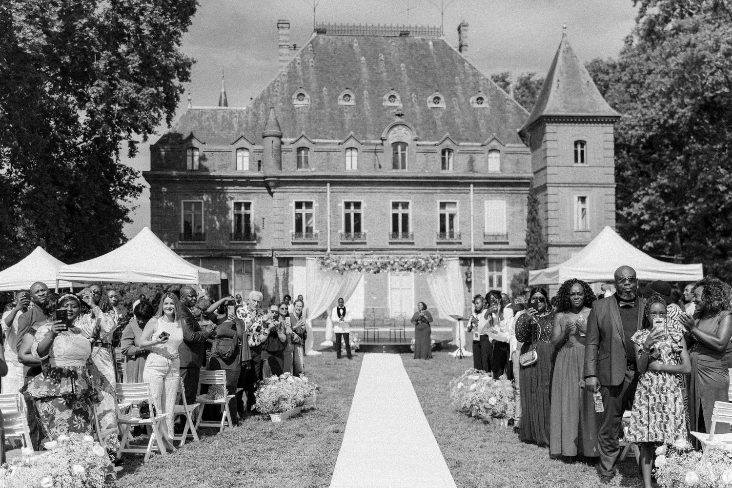 Panoramic view of a historic chateau with wedding guests gathered on the lawn during an outdoor celebration.