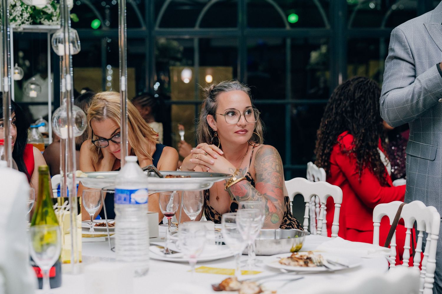 Wedding guests enjoy an elegant dinner reception with long tables decorated with floral centerpieces and string lights.