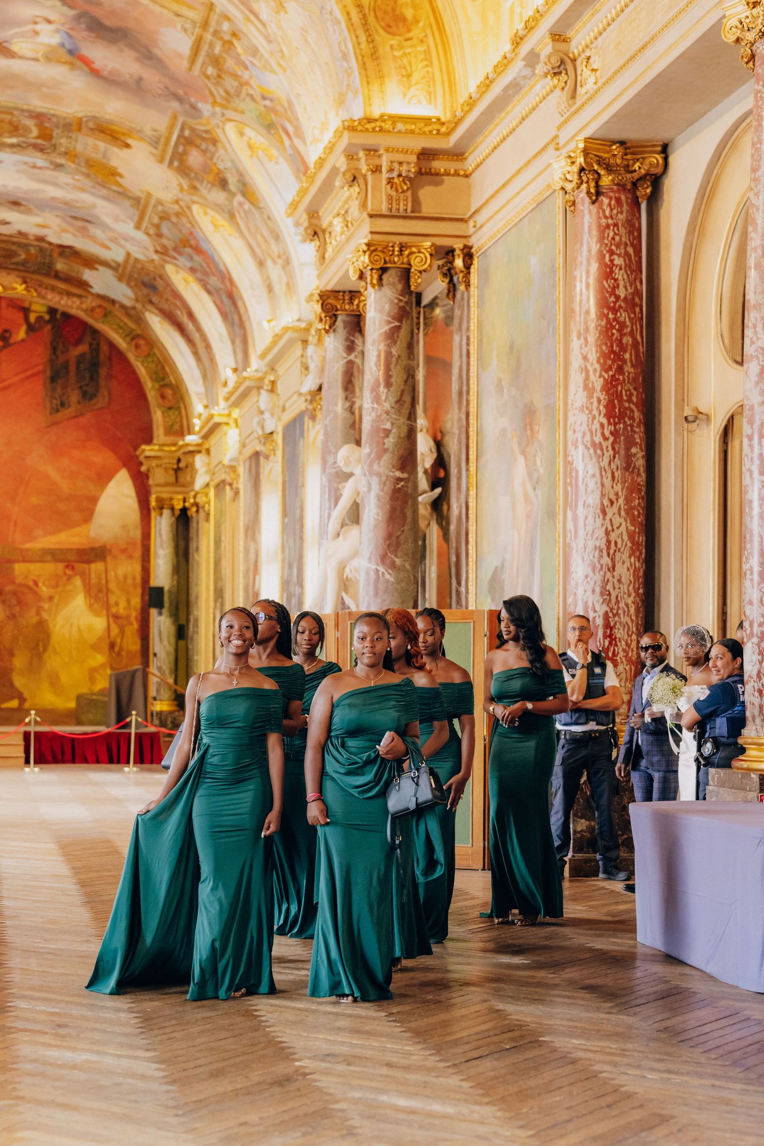Wedding party in emerald green dresses poses in an elegant baroque palace hall with golden details.